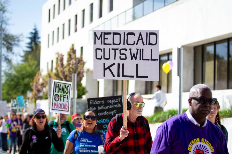 A person outside in a crowd holds a sign that says "Medicaid cuts will kill"